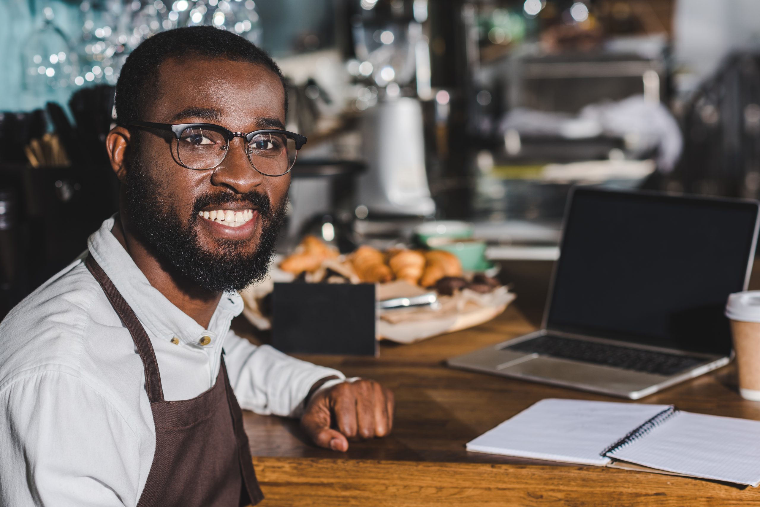 handsome young african american barista in eyeglasses smiling at camera while working in cafe